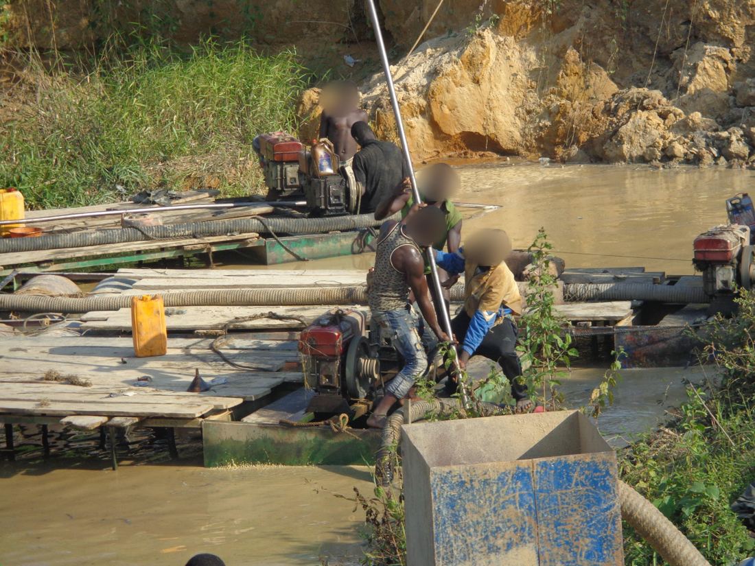 Several dredging rigs moored along an eroded riverbank with workers handling pipes and pumps