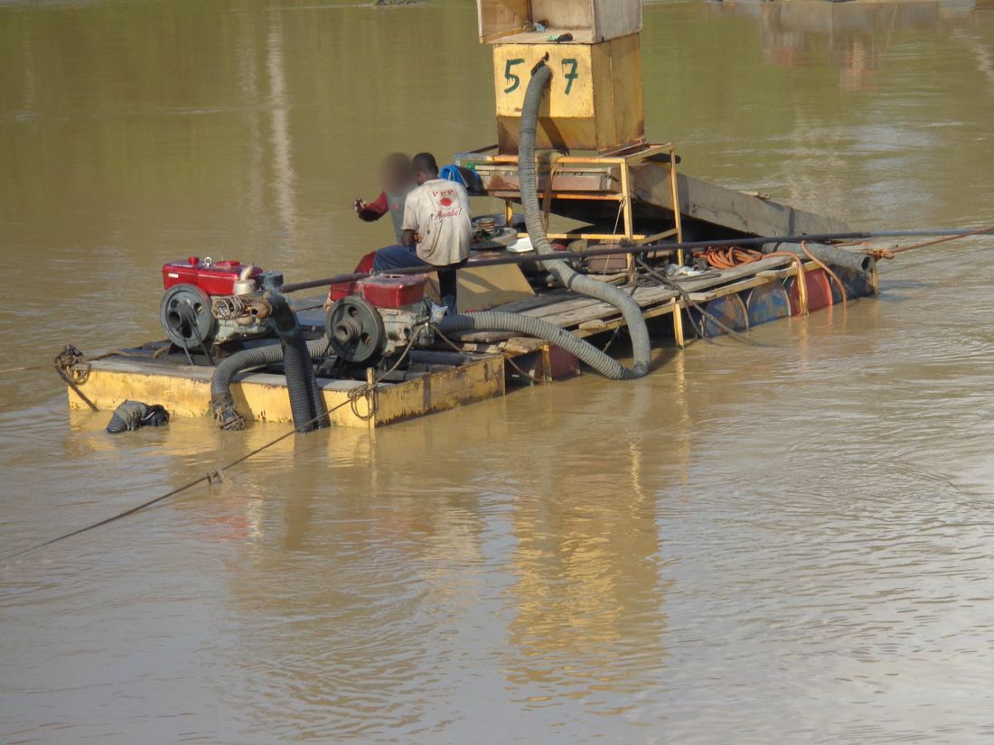 A floating dredging rig with engines and suction hoses on a muddy river